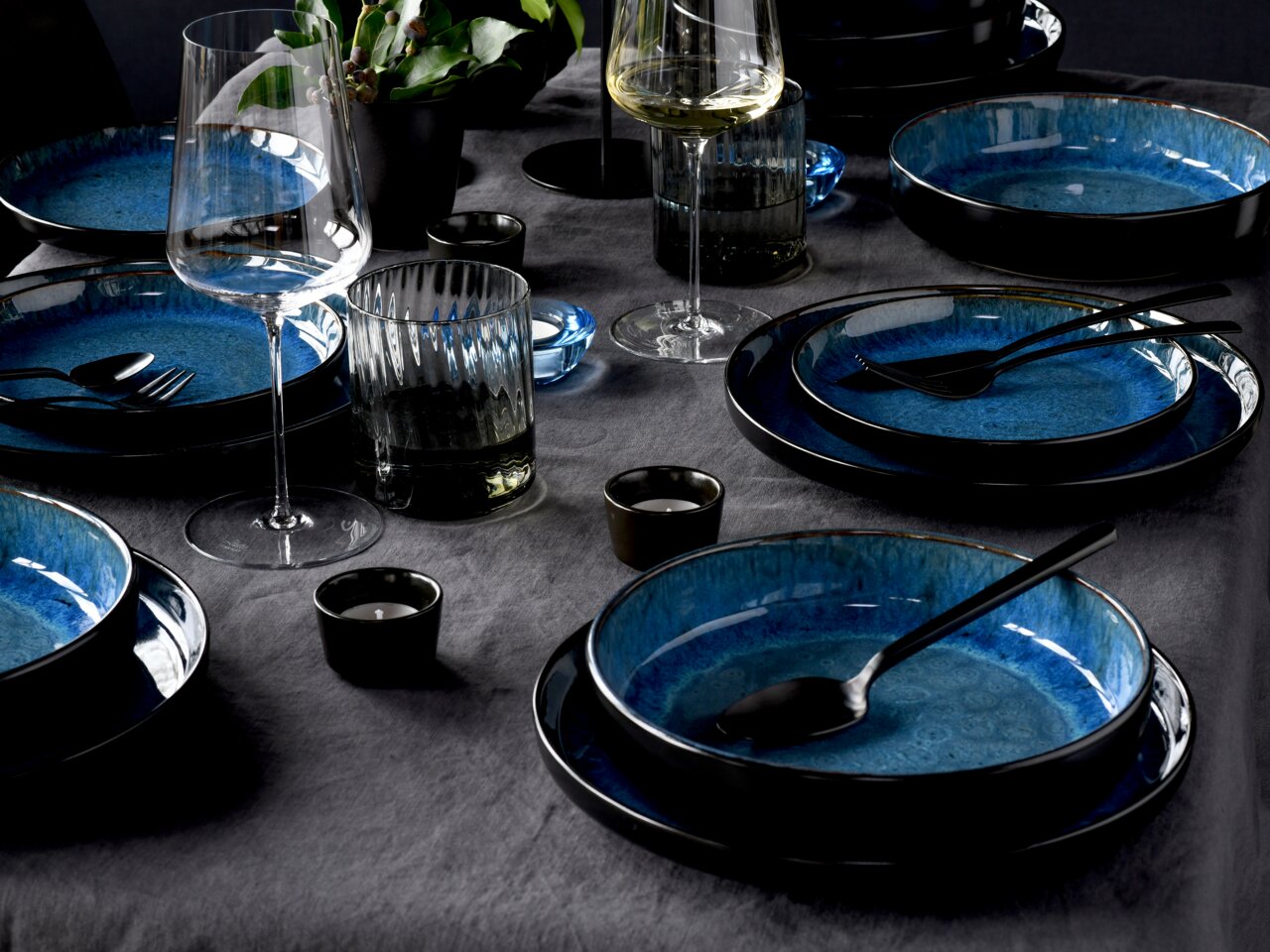 Elegantes 18-teiliges Tellerset in Blau, auf einem gedeckten Tisch mit Gläsern und Besteck, aus der Vogelperspektive fotografiert.