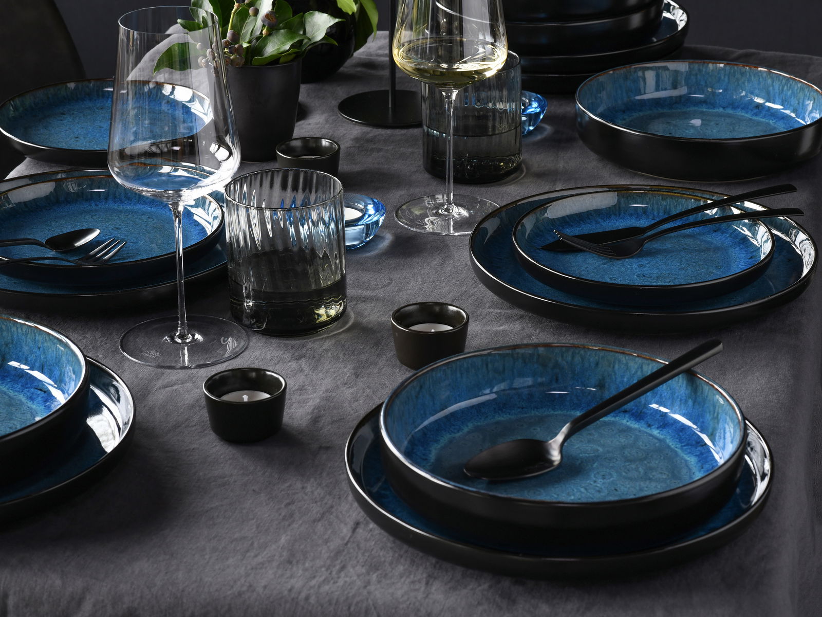 Elegantes 18-teiliges Tellerset in Blau, auf einem gedeckten Tisch mit Gläsern und Besteck, aus der Vogelperspektive fotografiert.