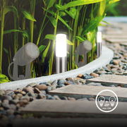 Gartenbeleuchtung mit Erdspießen, drei leuchtende Lampen entlang eines gepflasterten Weges, umgeben von Pflanzen, seitliche Perspektive