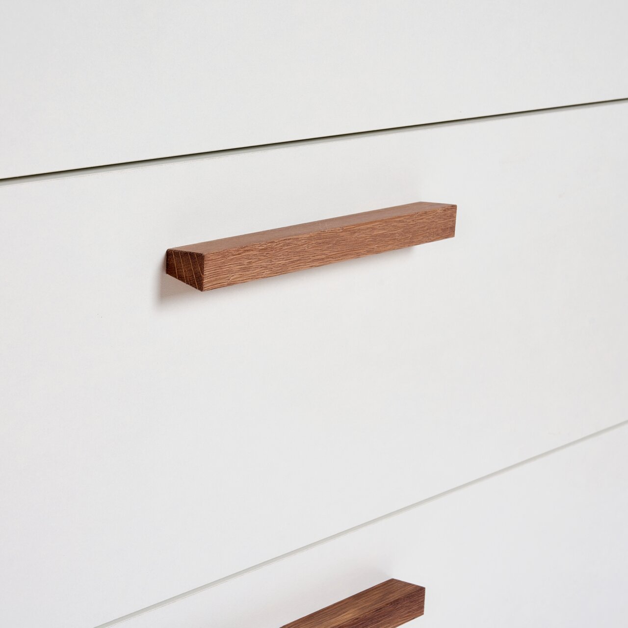 Close-up van een witte commode met houten handgrepen, gezien vanaf de zijkant