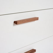 Close-up van een witte commode met houten handgrepen, gezien vanaf de zijkant