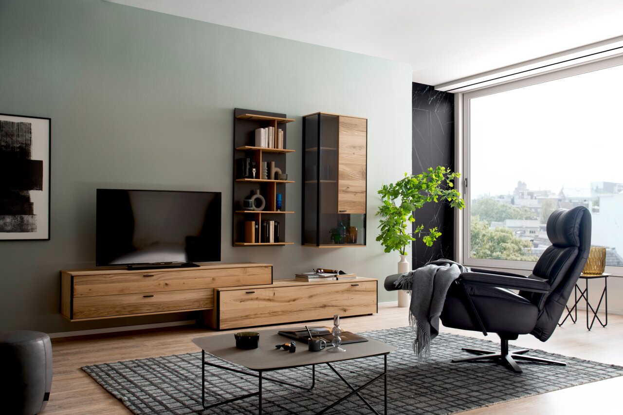 Moderner, drehbarer Relaxsessel in schwarzem Leder, seitliche Perspektive in einem stilvollen Wohnzimmer mit großen Fenstern.