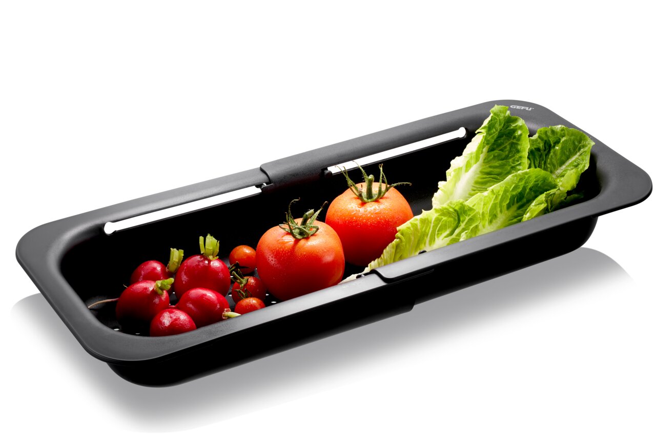 Zwarte gootsteenzeef van DRENARE met verse groenten, waaronder tomaten, radijsjes en slablaadjes, in zijaanzicht.