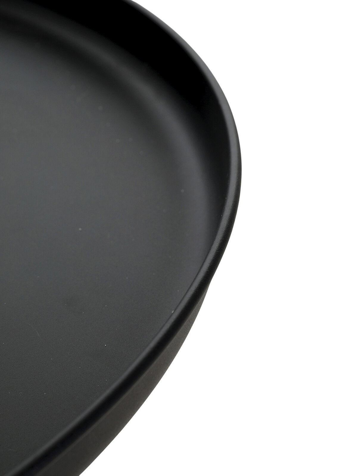 Schwarzer, runder Teller mit leicht erhöhtem Rand in Nahaufnahme, schräg von oben fotografiert.