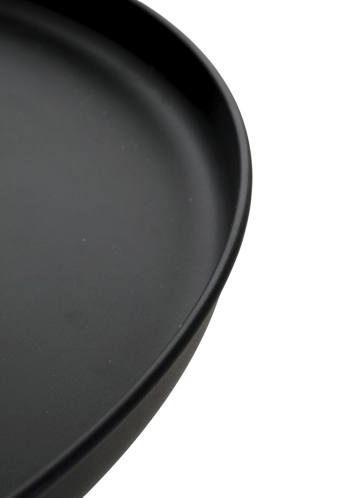 Schwarzer, runder Teller mit leicht erhöhtem Rand in Nahaufnahme, schräg von oben fotografiert.