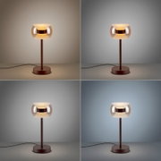 Moderne Tischleuchte mit rundem Glas-Schirm und warmem Licht, brauner Metallfuß und Kabel sichtbar, frontal aus leicht erhöhter Perspektive auf neutralem Hintergrund