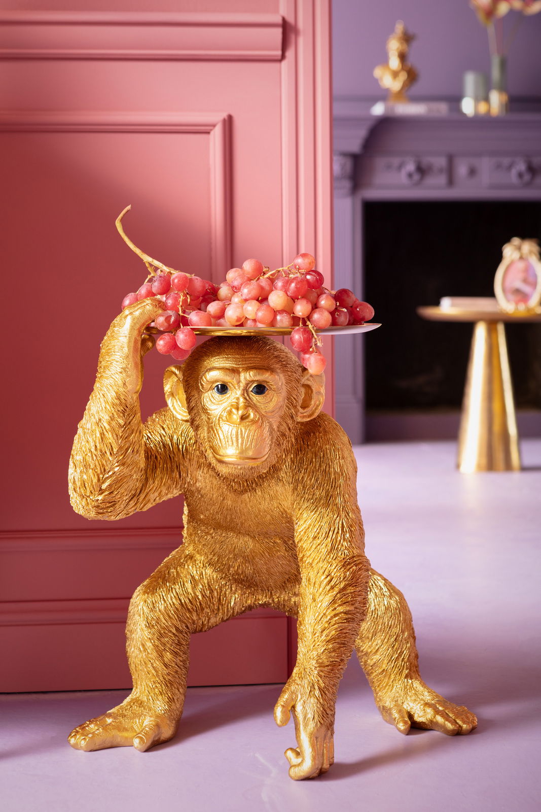 Goldene Deko-Figur eines Affen in Butler-Pose, der ein Tablett mit Trauben auf dem Kopf balanciert, seitliche Perspektive.