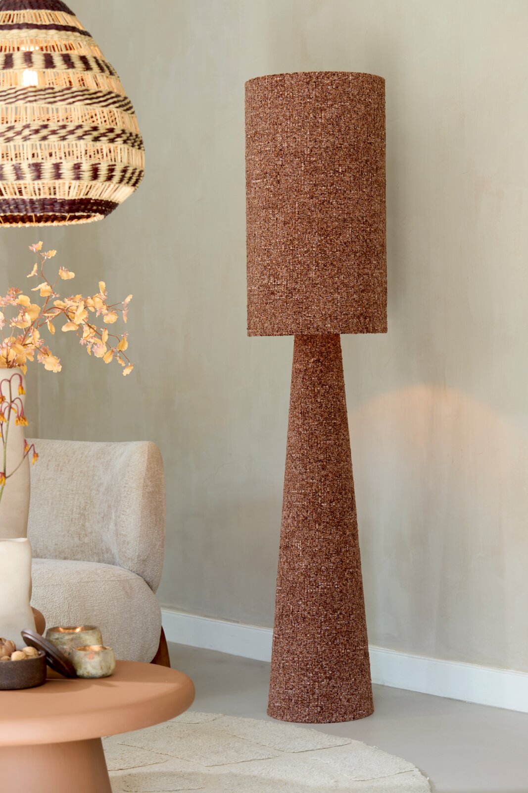 Vooraanzicht van een hoge bruine vloerlamp met taps toelopende voet en cilindervormige stoffen lampenkap in een sfeervol interieur