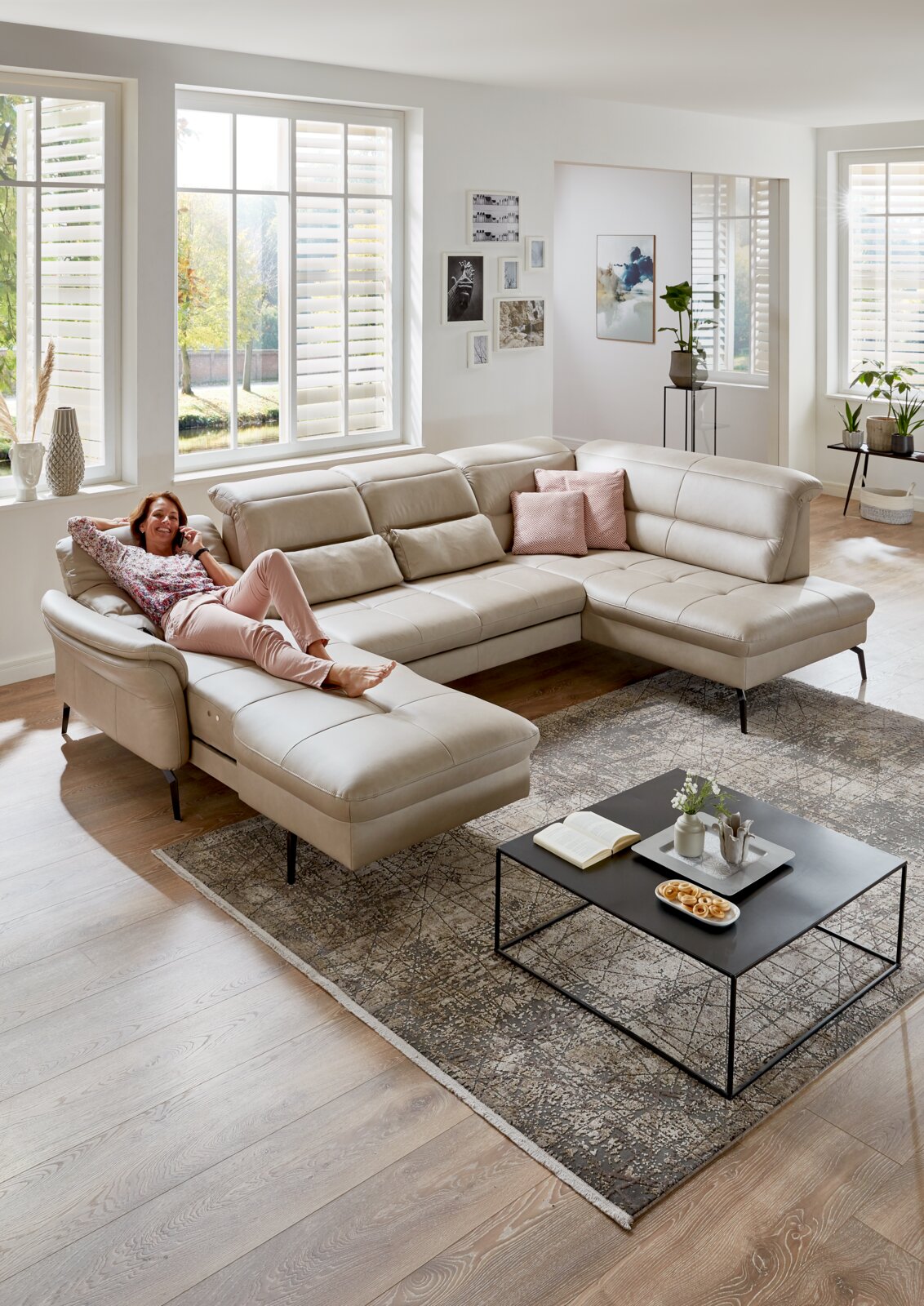 Een moderne gestoffeerde hoekbank in een lichte woonkamer, gezien van bovenaf, met een ontspannen persoon aan de linkerkant.