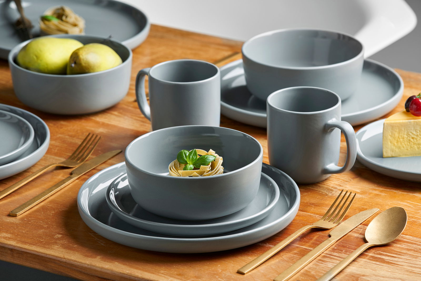 Graues Kombiservice 16-teilig Linz auf einem Holztisch, bestehend aus Tellern, Schalen und Tassen, mit goldfarbenem Besteck, aus der Vogelperspektive fotografiert.