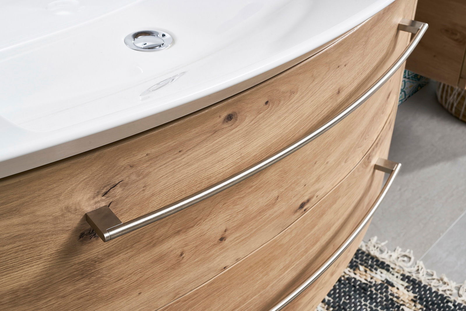 Nahaufnahme einer Badkombination mit Holzoptik und geschwungenen Metallgriffen, von der Seite betrachtet.