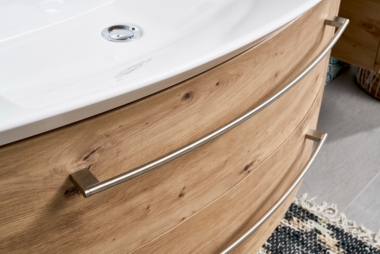 Nahaufnahme einer Badkombination mit Holzoptik und geschwungenen Metallgriffen, von der Seite betrachtet.