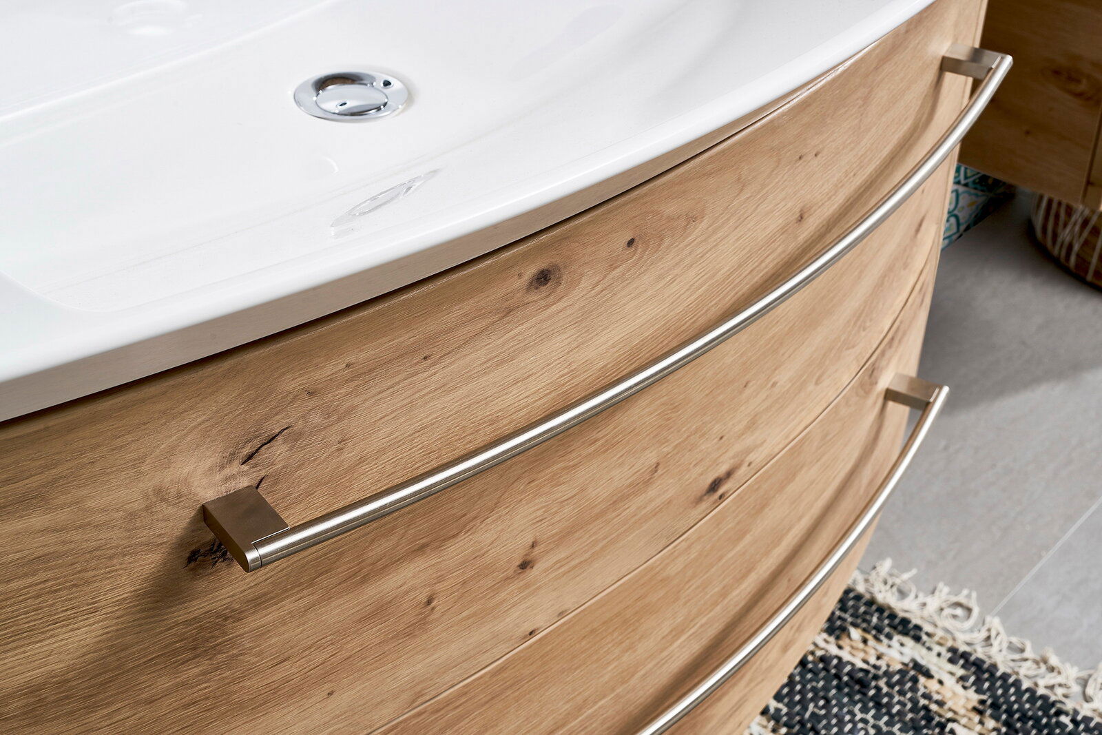 Nahaufnahme einer Badkombination mit Holzoptik und geschwungenen Metallgriffen, von der Seite betrachtet.