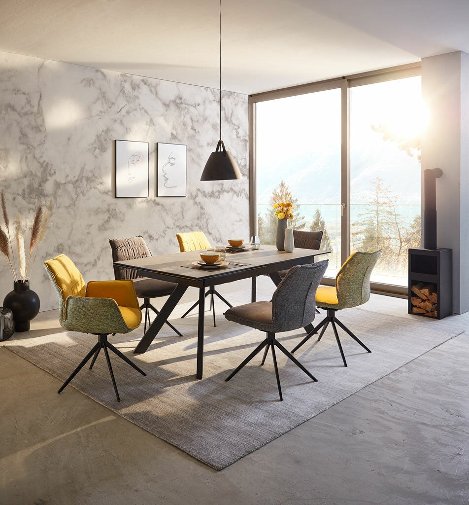 Moderner Esstisch mit stilvollen Stühlen in einem hellen Raum mit Blick auf die Berge, seitliche Perspektive.