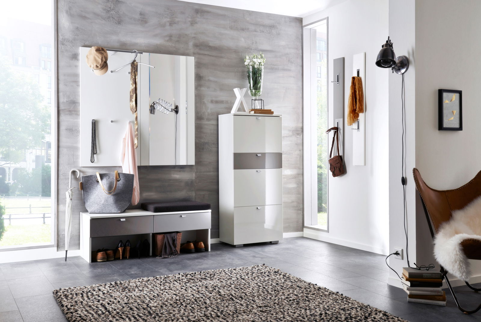 Moderne Garderobe in einem hellen Raum mit grauer Wand, bestehend aus einem weißen Schrank, einer Sitzbank mit Stauraum und Wandhaken. Perspektive von vorne.