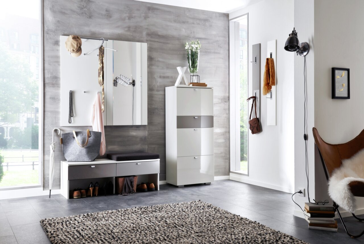 Moderne Garderobe in einem hellen Raum mit grauer Wand, bestehend aus einem weißen Schrank, einer Sitzbank mit Stauraum und Wandhaken. Perspektive von vorne.