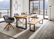 Moderner Esstisch aus Holz mit Metallbeinen, umgeben von grauen Stühlen und einer Bank, in einem hellen Raum mit Blick auf einen See. Perspektive: seitlich.