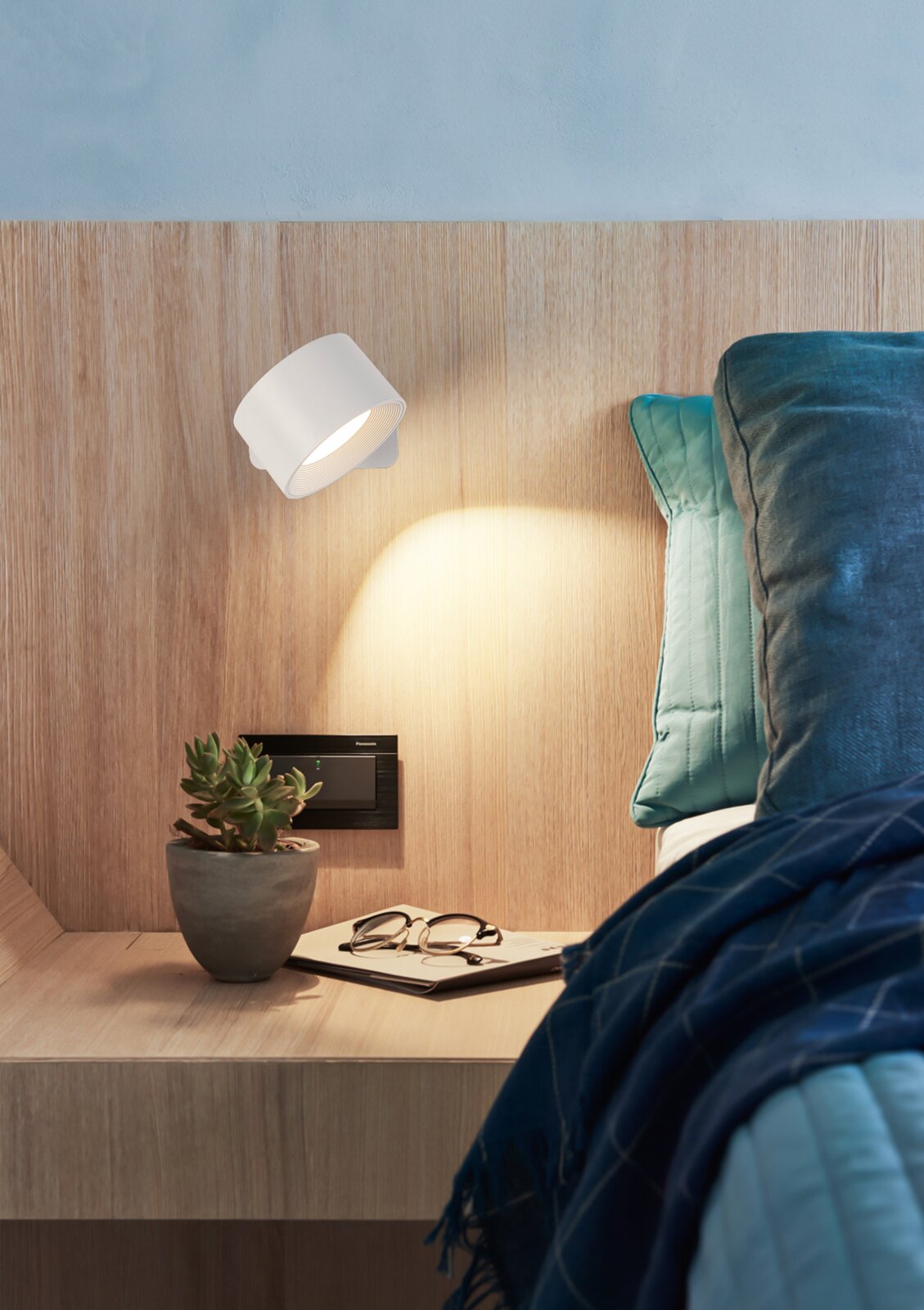 Weiße, moderne LED-Wandleuchte als Leselampe am Holz-Kopfteil über dem Nachttisch, seitliche Perspektive im Schlafzimmer