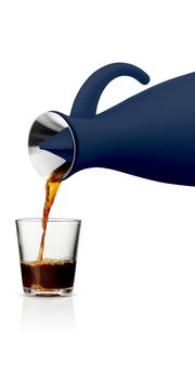 Navy blaue Isolierkanne, die aus seitlicher Perspektive Kaffee in ein Glas gießt.