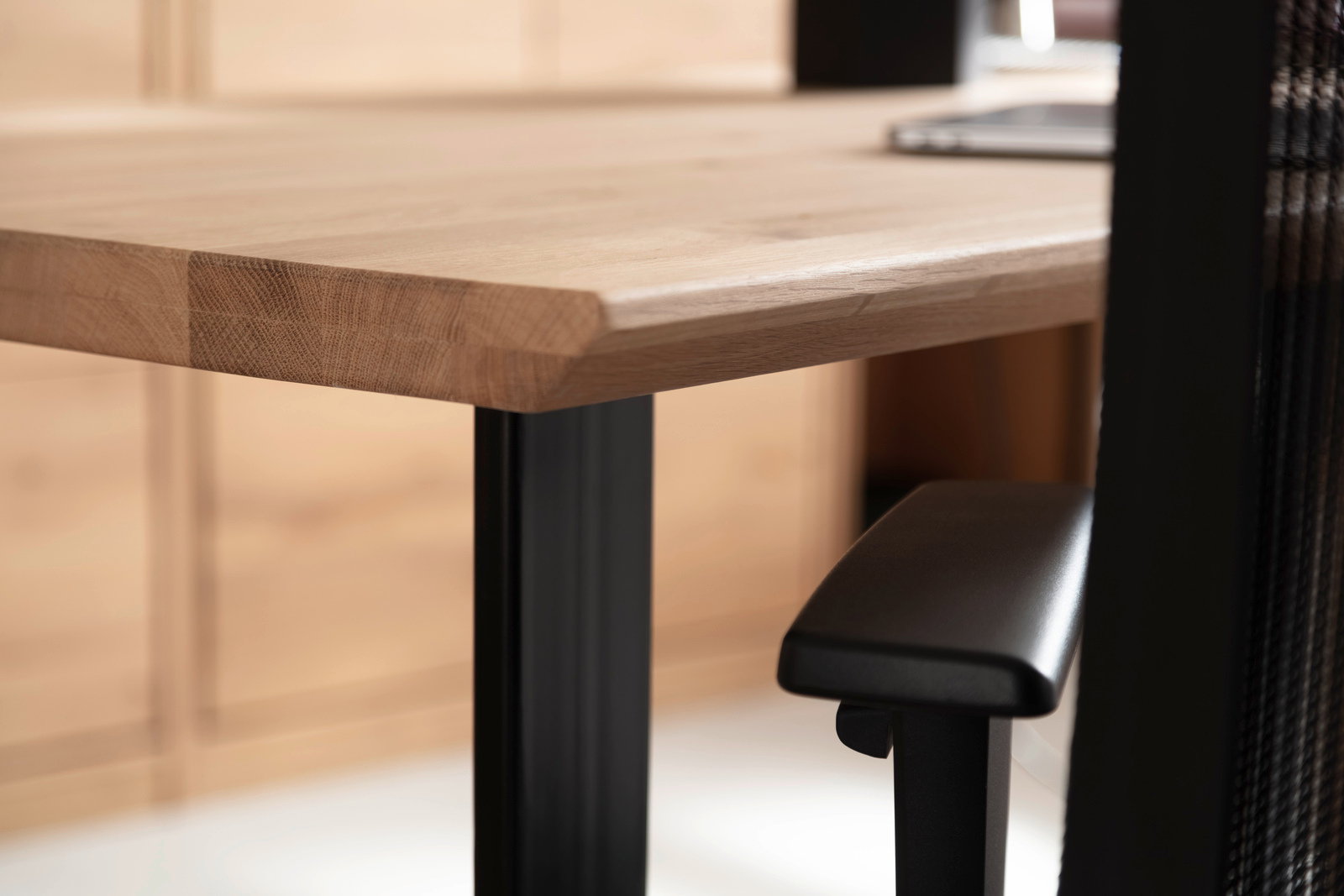 Nahaufnahme eines Schreibtisches mit Holzplatte und schwarzem Metallgestell, seitliche Perspektive