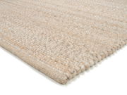 Nahaufnahme eines handgewebten Teppichs in neutralen Beigetönen, perspektivisch von der Seite aufgenommen.