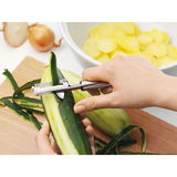 Nahaufnahme eines Pendelschälers PROFI PLUS, der eine Gurke schält. Der Schäler wird von einer Hand gehalten und zeigt die Funktionalität des Produkts.