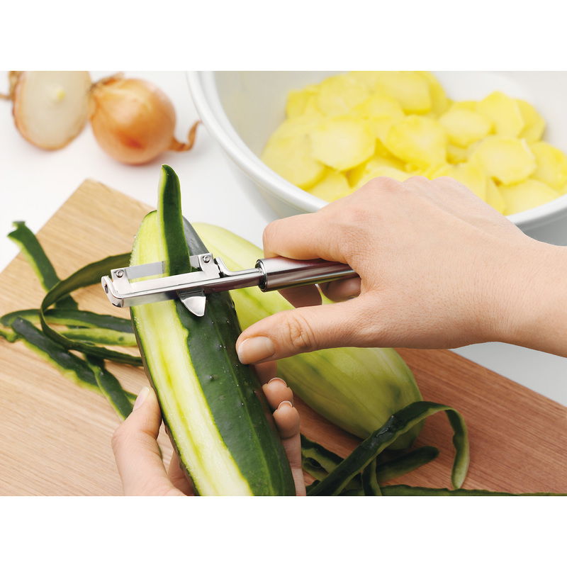 Nahaufnahme eines Pendelschälers PROFI PLUS, der eine Gurke schält. Der Schäler wird von einer Hand gehalten und zeigt die Funktionalität des Produkts.