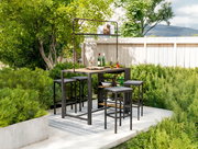 Bar-Set im Garten mit Tisch und Hockern, umgeben von grünen Pflanzen, aus der Perspektive von vorne.
