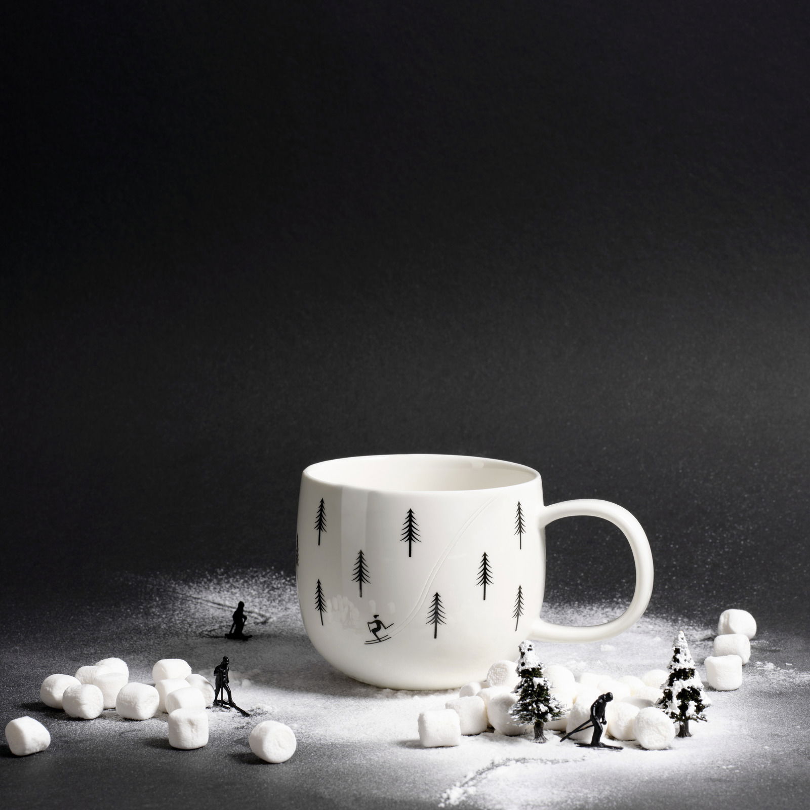 ASA SELECTION Henkelbecher JOY XMAS Weißer Henkelbecher mit Skifahrer- und Tannenbaum-Motiv, umgeben von Miniatur-Skifahrern und Marshmallows, seitliche Perspektive