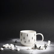 Weißer Henkelbecher mit Skifahrer- und Tannenbaum-Motiv, umgeben von Miniatur-Skifahrern und Marshmallows, seitliche Perspektive