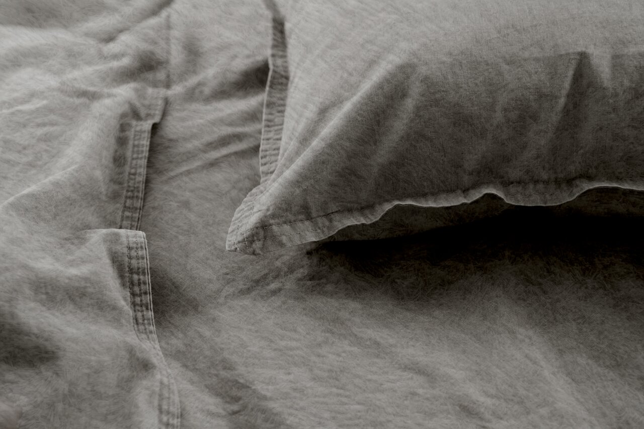 Graue Bettwäsche mit Kissenbezug in Nahaufnahme, weiche Textur und dezente Falten