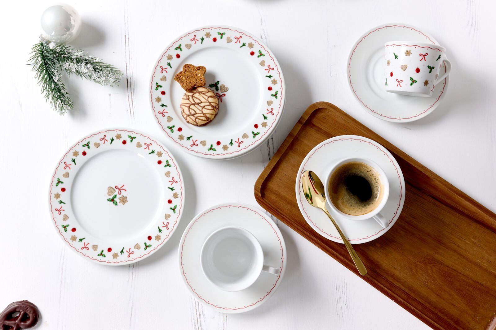 Kaffeeservice 18-tlg. mit festlichem Design, bestehend aus Tellern, Tassen und Untertassen, dekoriert mit weihnachtlichen Motiven wie Schleifen und Sternen, aus der Vogelperspektive fotografiert.