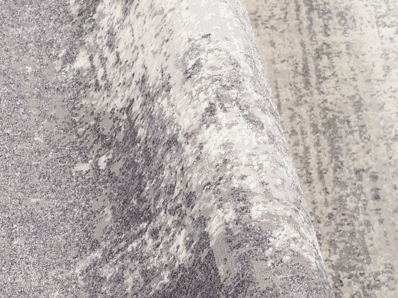 Nahaufnahme eines Designer Teppichs in Grau- und Weißtönen mit abstraktem Muster, perspektivisch von der Seite aufgenommen.