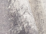 Nahaufnahme eines Designer Teppichs in Grau- und Weißtönen mit abstraktem Muster, perspektivisch von der Seite aufgenommen.