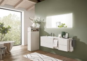 Modernes Badezimmer mit weißem, schwebendem Waschtisch mit Schubladen und Aufsatzwaschbecken, hohem Badschrank und Wandspiegel vor salbeigrüner Wand; Perspektive: frontale, leicht seitliche Raumansicht.
