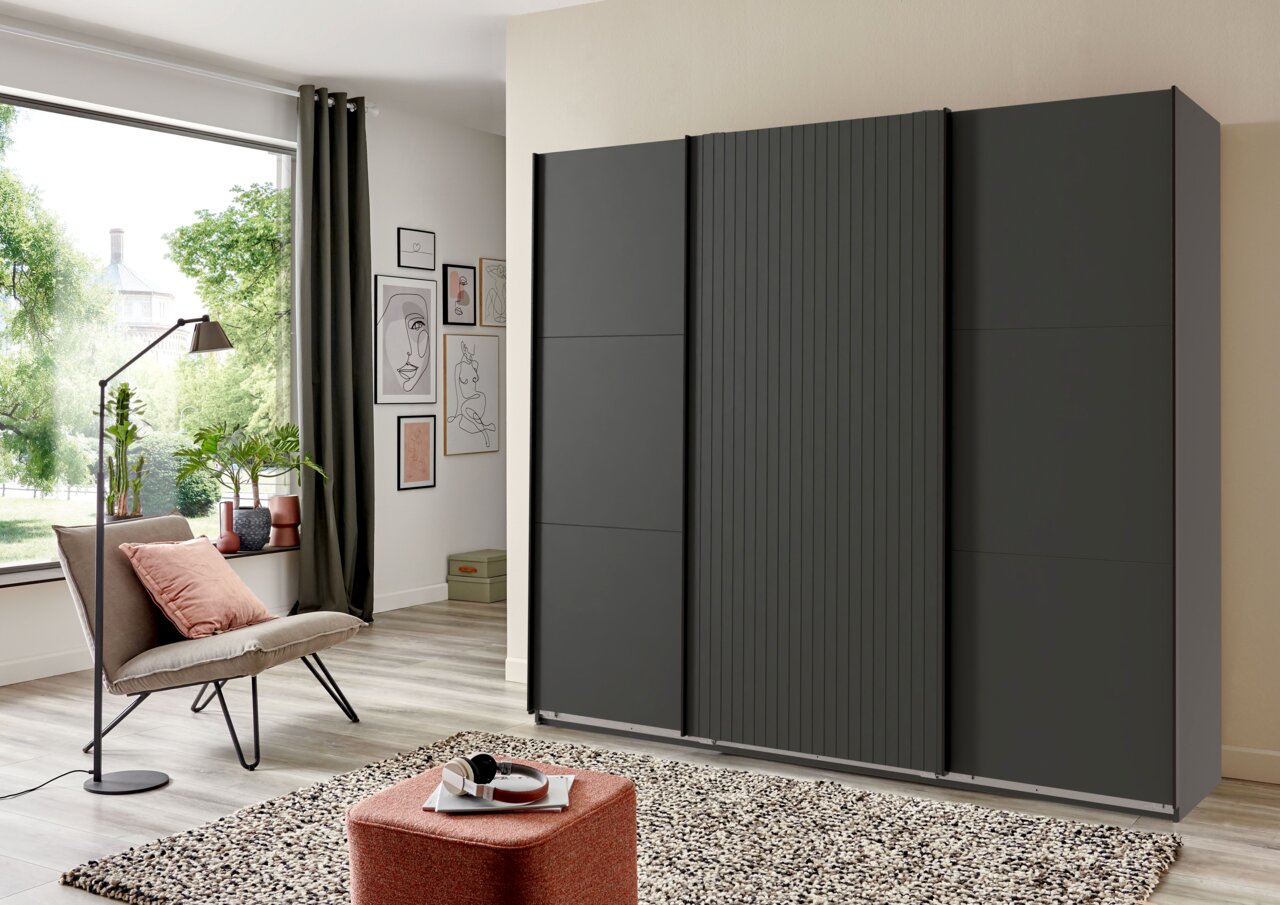 Moderne drievleugelige kast met zweefdeuren in een donkere uitvoering, zijaanzicht in een stijlvolle woonkamer.