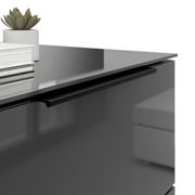 Nahaufnahme einer modernen Nachtkommode mit glänzender Oberfläche, schwarzem Griff und dekorativen Elementen wie einem Buchstapel und einer kleinen Pflanze.