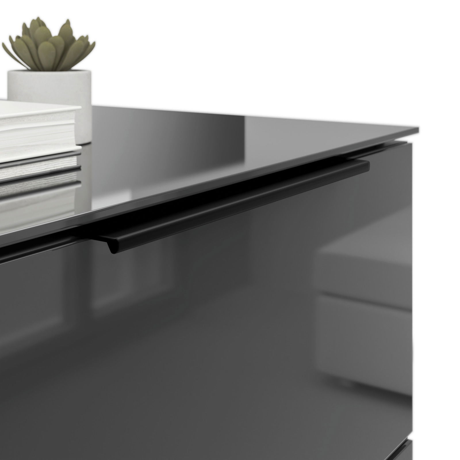 Nahaufnahme einer modernen Nachtkommode mit glänzender Oberfläche, schwarzem Griff und dekorativen Elementen wie einem Buchstapel und einer kleinen Pflanze.