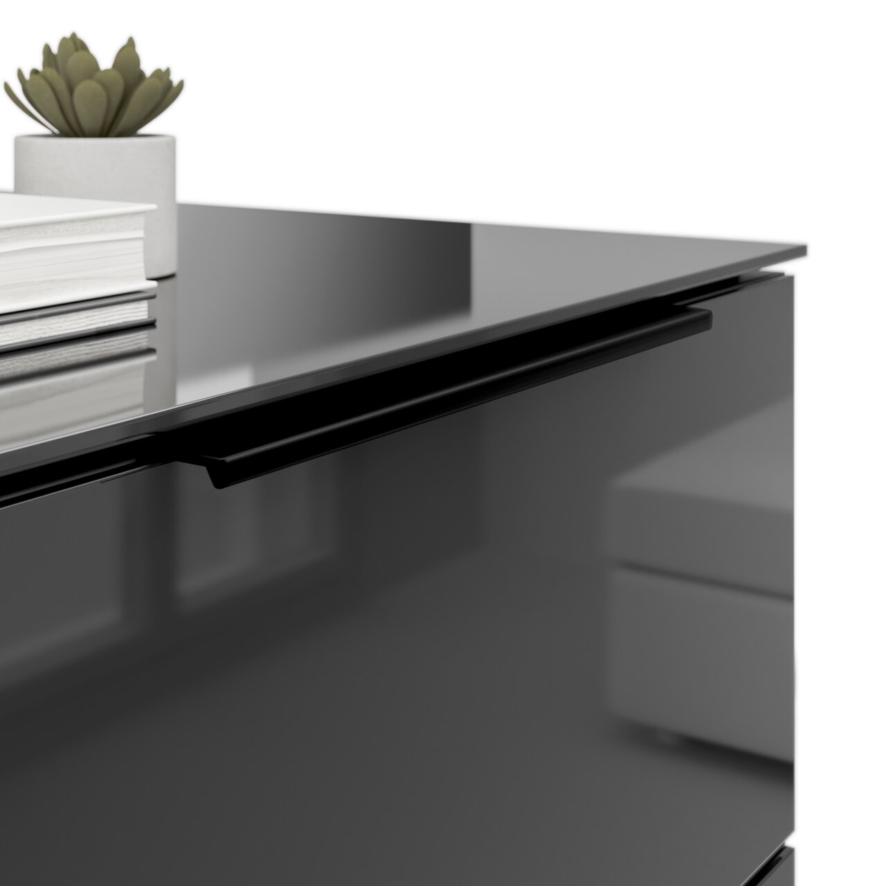 Close-up van een modern nachtkastje met een glanzend oppervlak, een zwarte handgreep en decoratieve elementen zoals een stapeltje boeken en een plantje.