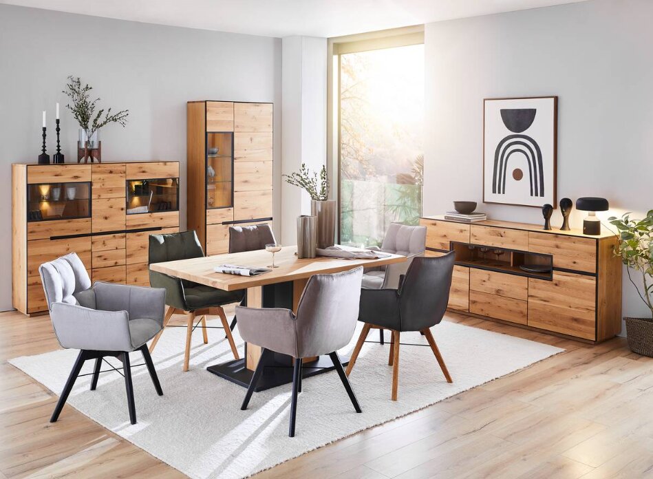 Esszimmer mit Holztisch und verschiedenen Armlehnenstühlen in einem modernen, hellen Raum mit Holzschränken und Dekorationen, seitliche Perspektive.