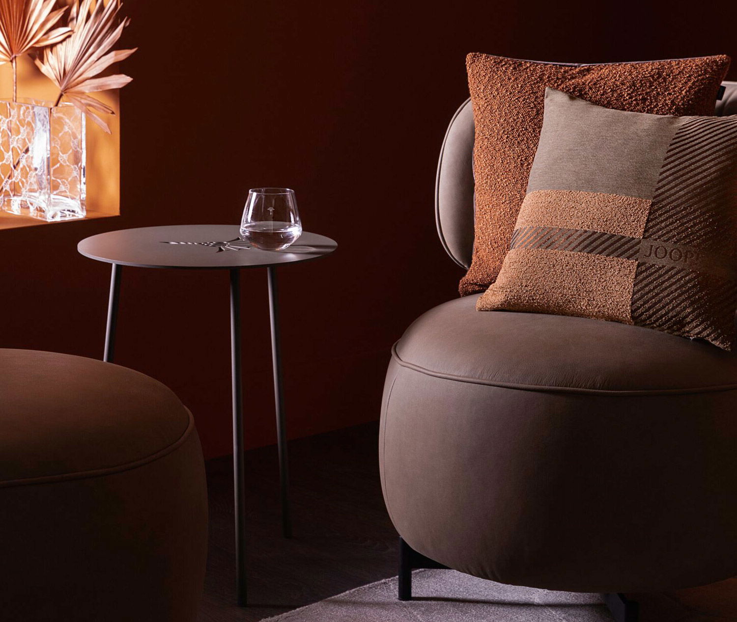 Grauer Ledersessel mit dekorativen Kissen und einem schwarzen Beistelltisch aus Metall vor einem warmen, dunklen Hintergrund.