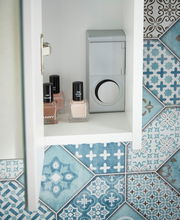 Innenansicht eines Spiegelschranks mit Nagellackflaschen und einer Steckdose, umgeben von dekorativen blauen Fliesen.