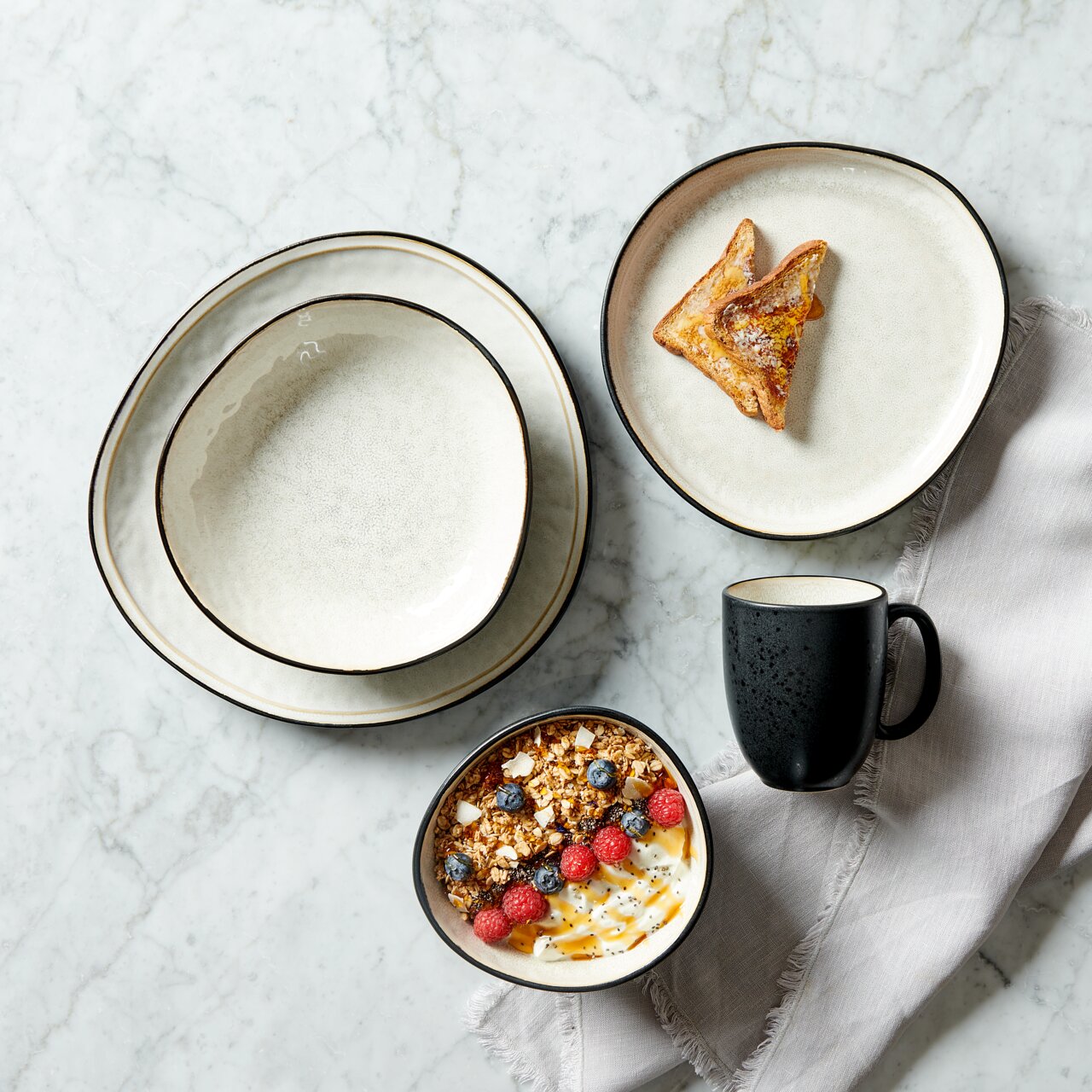 Vogelperspectief op een 10-delige servieset met borden, schaal en kopje in een elegant ontwerp op een marmeren tafel, versierd met toast en muesli.