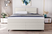 Frontale Ansicht eines eleganten Boxspringbetts mit hellem Stoffbezug, flankiert von modernen Nachttischen und stilvoller Dekoration.