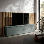 Modernes TV-Lowboard in mattem Grün mit zwei Schubladen und zwei Türen, seitliche Perspektive, im Wohnzimmer neben einem Fahrrad platziert.