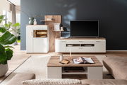 Moderne Wohnzimmer-Wandkombination in hellem Holz und Weiß, bestehend aus TV-Schrank, Vitrine und Regalen, aus der Perspektive eines gemütlichen Wohnzimmers mit Pflanzen und Dekoration.