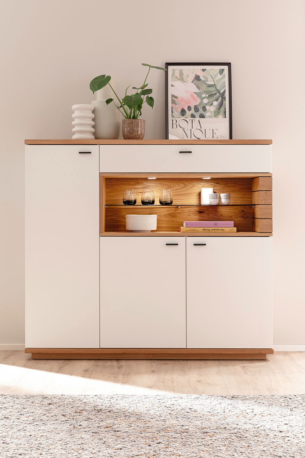 Modernes Highboard in Weiß mit Holzdetails, dekoriert mit Pflanzen und Kunst, aus frontaler Perspektive.