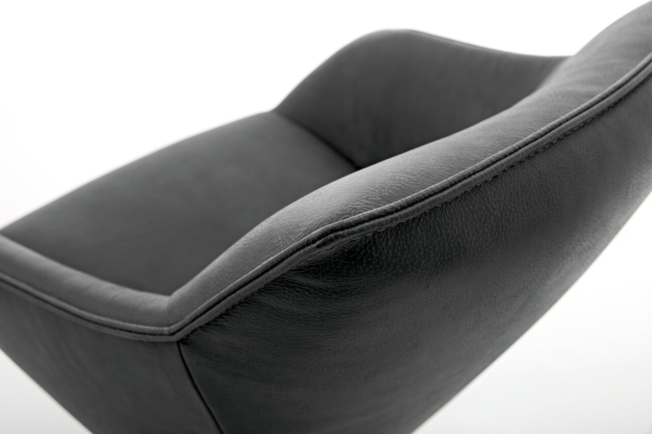 Nahaufnahme eines modernen, dunkelgrauen Sessels aus Leder mit geschwungenen Linien, seitliche Perspektive.