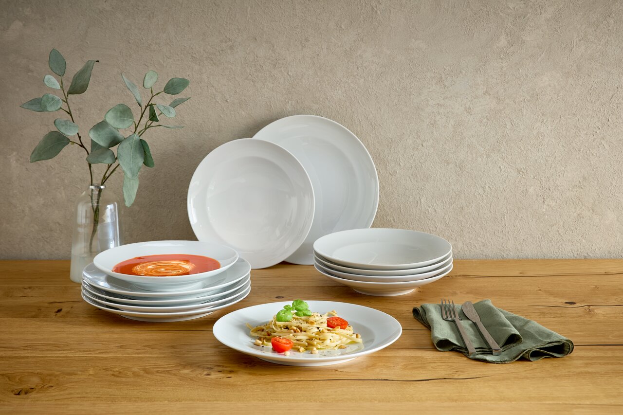 Seltmann Weiden Tafelservice 12-teilig LIBERTY DELUXE Weißes, schlichtes Porzellan-Geschirrset mit gestapelten Tellern und Schalen auf einem Holztisch, dekoriert mit Vase und Besteck; Perspektive: frontale Tischansicht auf Augenhöhe.