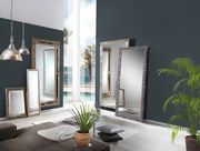 Mehrere große Spiegel mit dekorativen Rahmen in einem modernen Wohnzimmer, mit Blick auf einen Pool und Palmen durch ein großes Fenster.